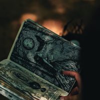 A hand holding a book with mystical illustrations, captured in artistic lighting.