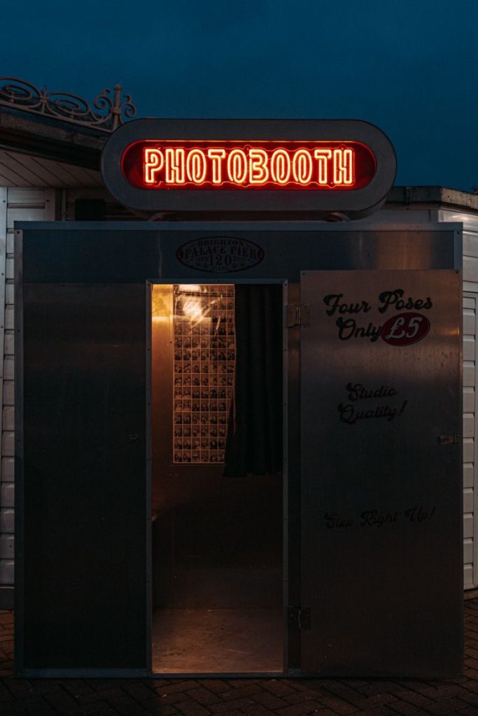 A neon-lit photobooth entrance captured against the night sky in Brighton, England.