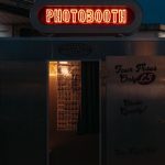 A neon-lit photobooth entrance captured against the night sky in Brighton, England.