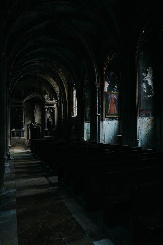 Dimly lit, eerie interior of an abandoned church with gothic arches and shadows.