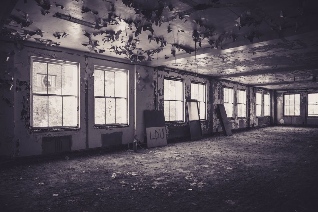 A dimly lit abandoned room with peeling paint and broken windows, creating a haunting atmosphere.