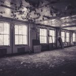 A dimly lit abandoned room with peeling paint and broken windows, creating a haunting atmosphere.