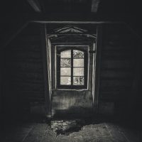 A haunting monochrome image of an abandoned attic, featuring a broken window and eerie shadows.