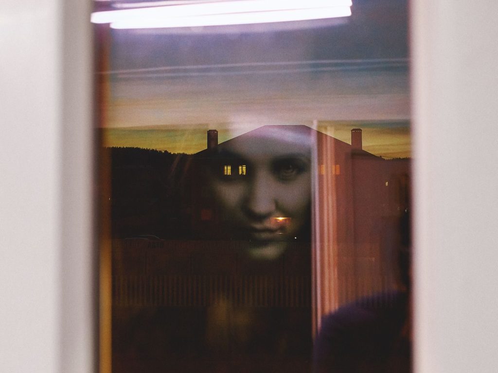 A haunting reflection of a woman's face appears in the window at twilight.