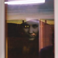 A haunting reflection of a woman's face appears in the window at twilight.