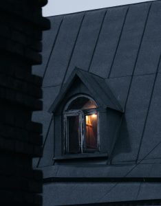 Dramatic view of a rooftop window emitting soft light against the evening sky.
