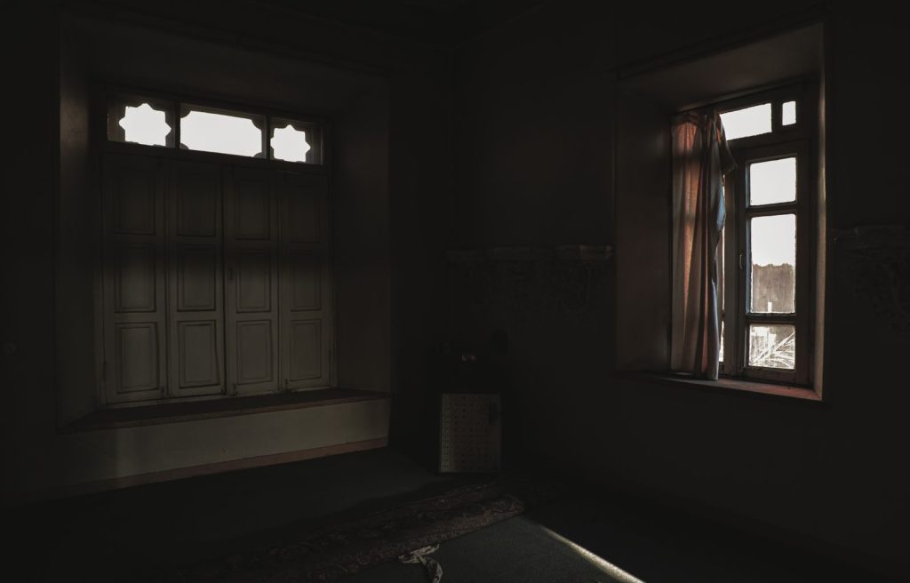 Dark room with open windows casting soft light and shadows creating a moody atmosphere.