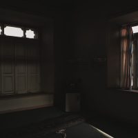 Dark room with open windows casting soft light and shadows creating a moody atmosphere.