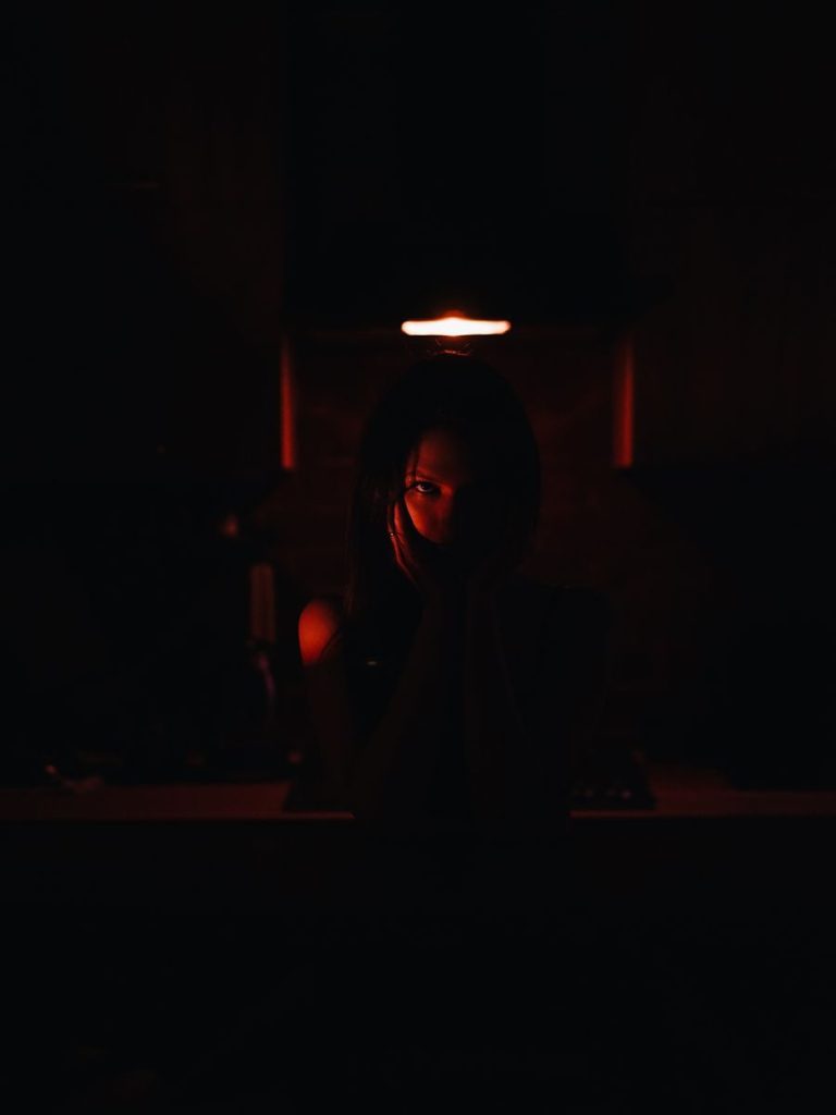 A mysterious silhouette of a woman in a dimly lit room with red lighting creating a haunting atmosphere.