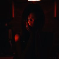 A mysterious silhouette of a woman in a dimly lit room with red lighting creating a haunting atmosphere.