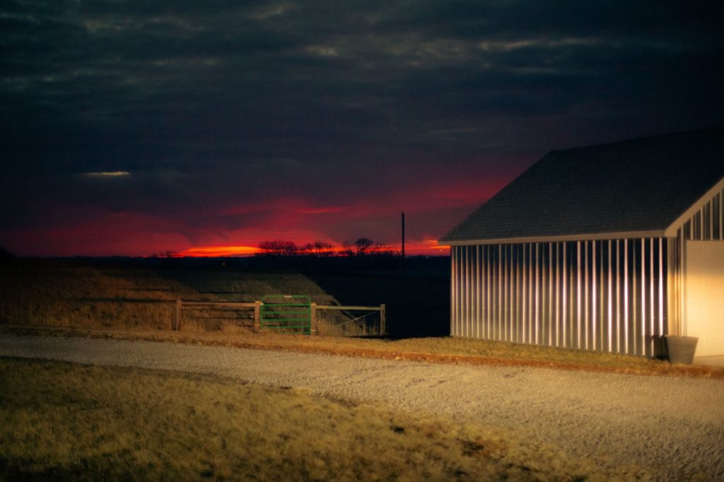 Peaceful countryside scene with a dramatic sunset over a farmhouse and gravel road.