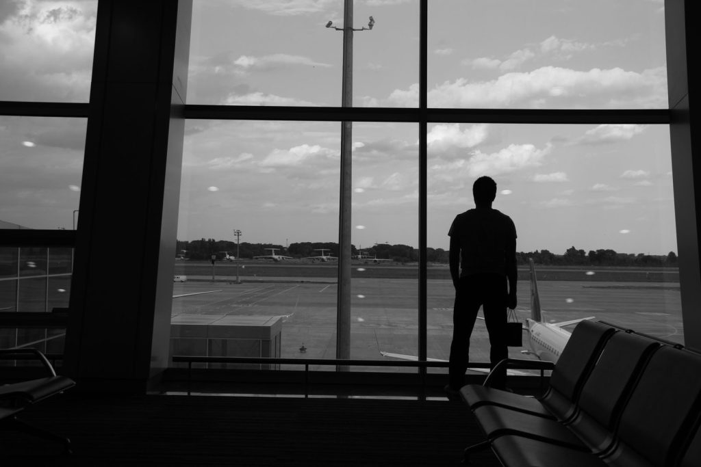 A silhouette of a man standing at an airport terminal window, looking onto the tarmac.