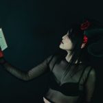 Artistic portrait of a woman in a horned costume holding a book, evoking a dark fantasy theme.